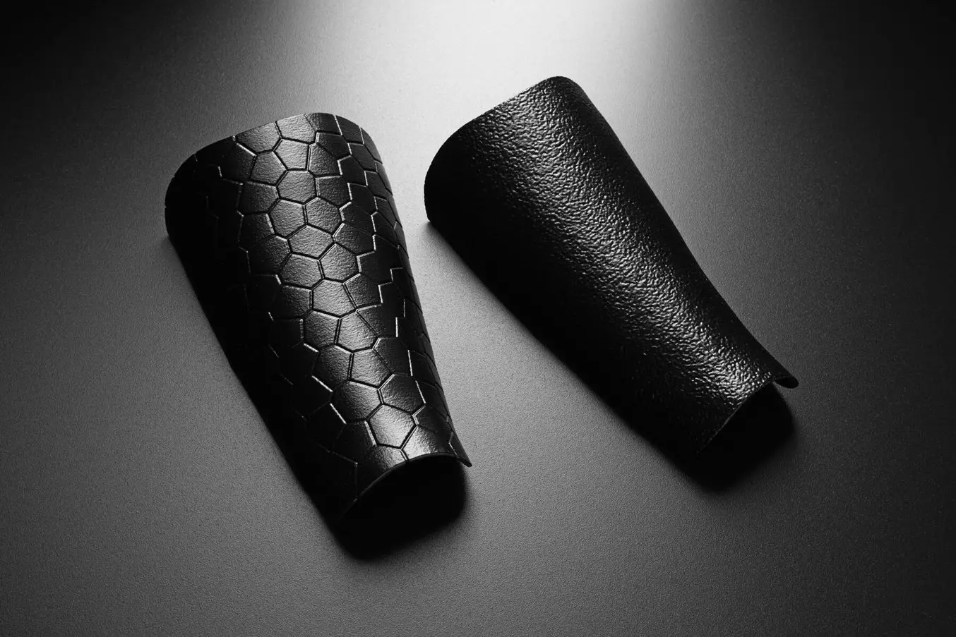 Two black 3D printed parts, one with a hexagonal print and one with light texturing