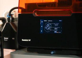 Close up on the touchscreen of a Form 3+ 3D printer showing Japanese labels. In the background is a 5 L resin container.