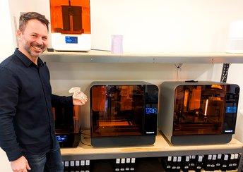 Man holding a 3D printed bolus device stands next to Form 3 series printers.