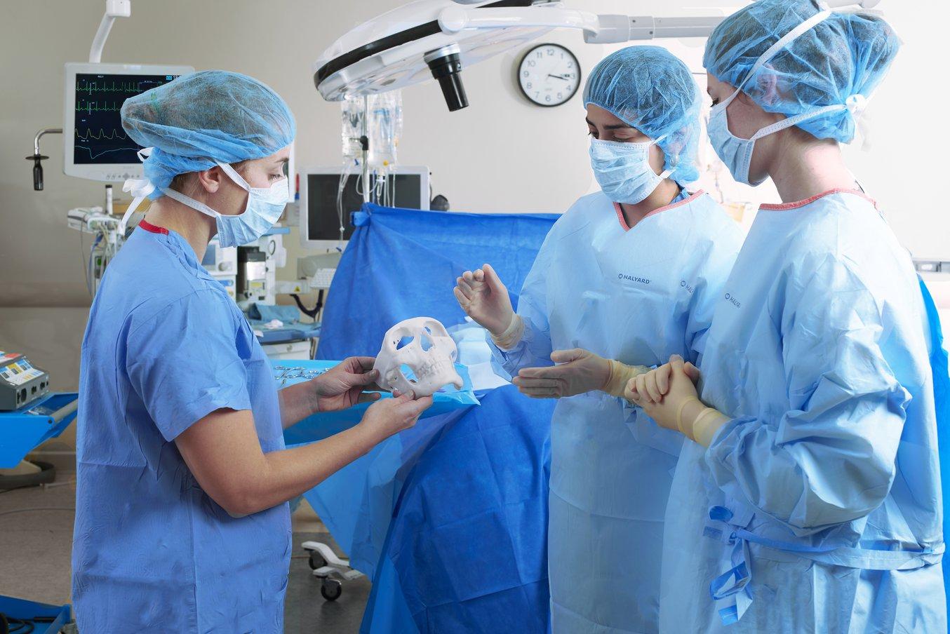 Three medical professions in PPE stand in an operating room holding an anatomical model
