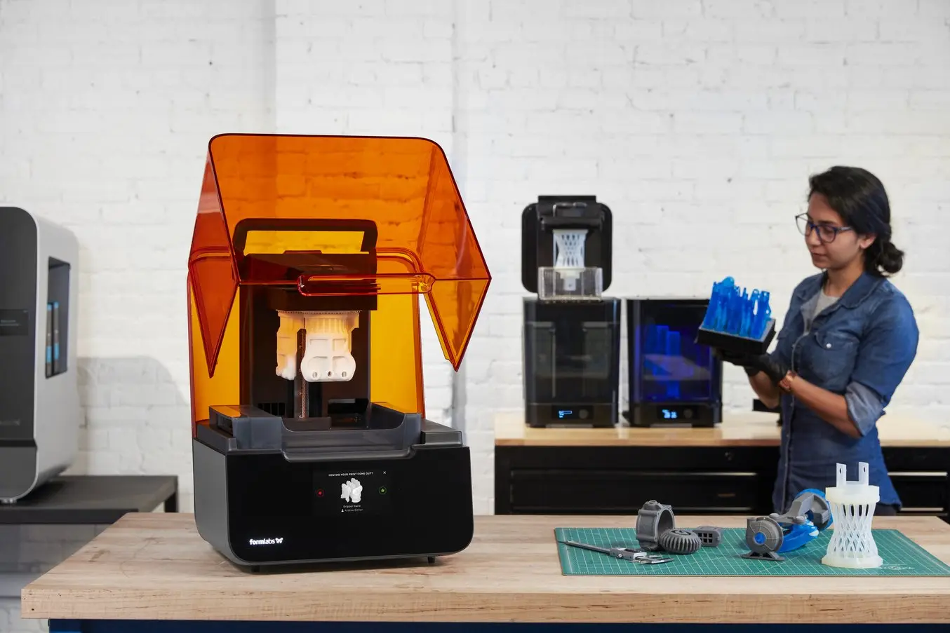 une imprimante stéréolithographique SLA Form 3+ sur un bureau avec des pièces imprimées en 3D
