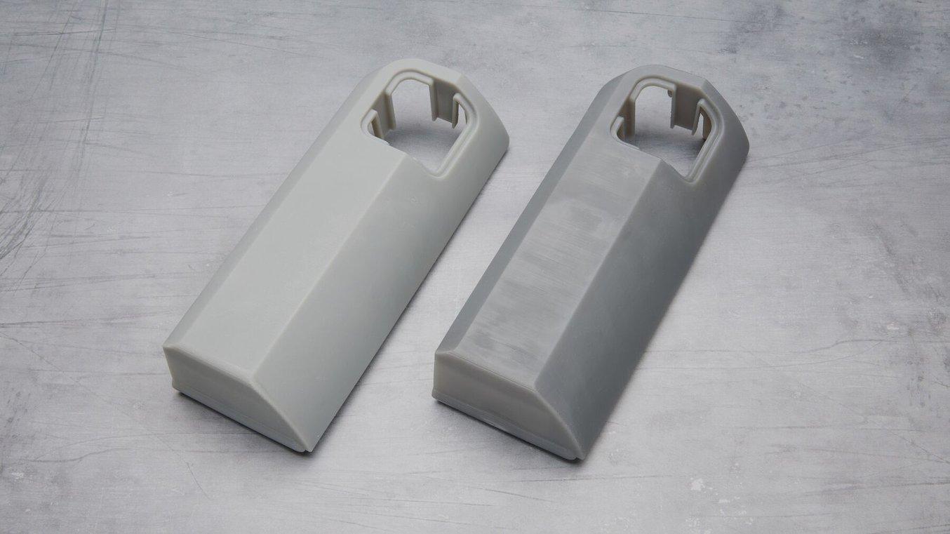 3Dプリント製の2つのグレーパーツ。写真左のパーツは、右のパーツより明るい灰色でマットな質感も増している。