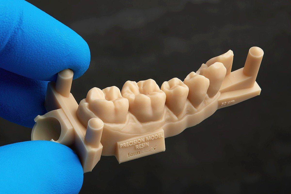 un cuadrante de arcada dental impreso en la Form 4 con la Precision Model Resin, sostenido por dos dedos con un guante azul sobre un fondo oscuro