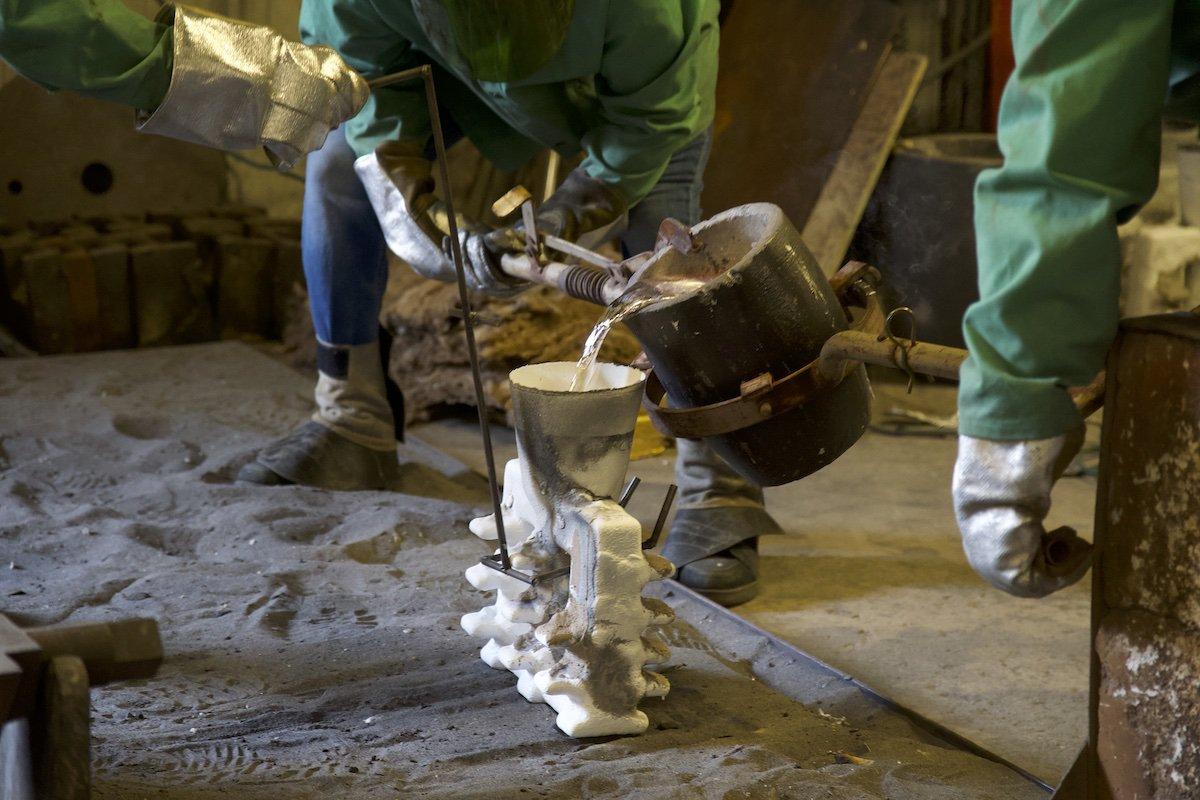 two men pour molten metal into an investment cast