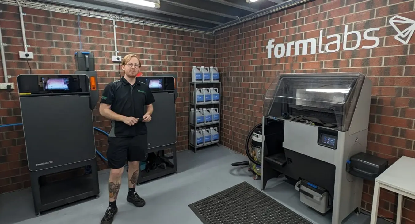 Person standing in front of two Fuse 1+ 30W 3D printers, shelf of powder, and Fuse Sift