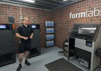 Person standing in front of two Fuse 1+ 30W 3D printers, shelf of powder, and Fuse Sift