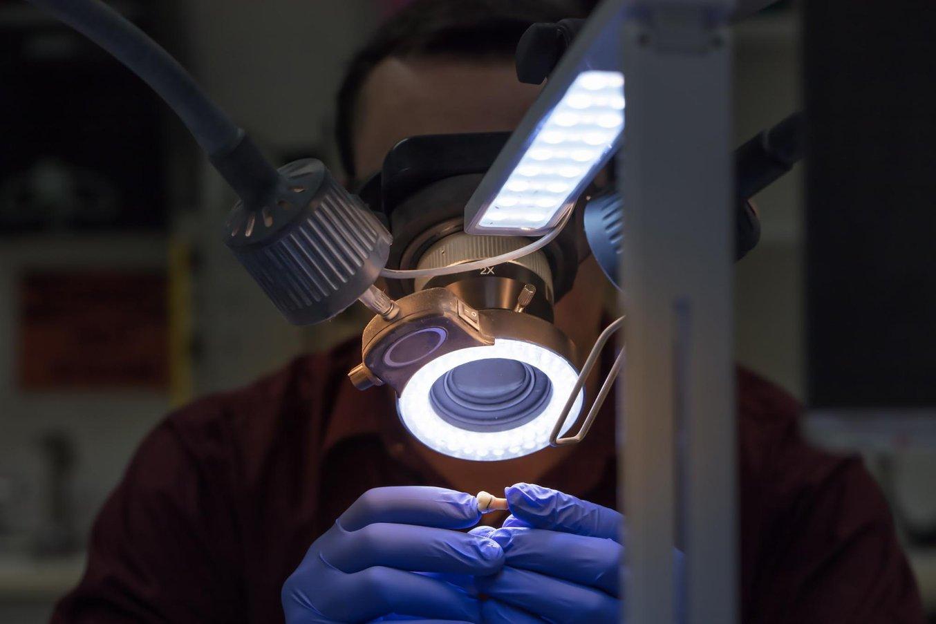 Dental professional examining a die model under a light and lens.
