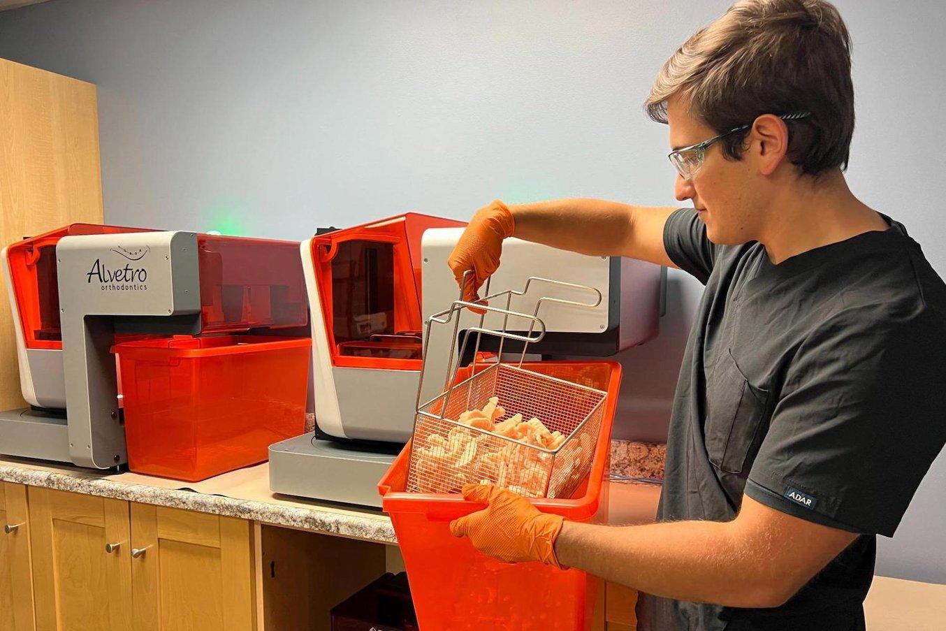 Une personne retire un panier de modèles imprimés en 3D d'un bac situé à côté des imprimantes Form 3B+ et Form Auto 
