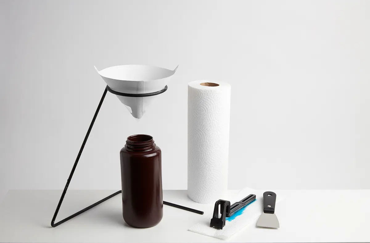作業台で必要な備品:リングスタンドが付いた不透明なプラスチックの容器とその上に吊るす未使用の塗料フィルタ、ペーパータオル、ワイパー、ならびに角が丸くなっているヘラ。