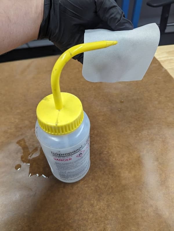Wetting a non-abrasive wipe with isopropyl alcohol