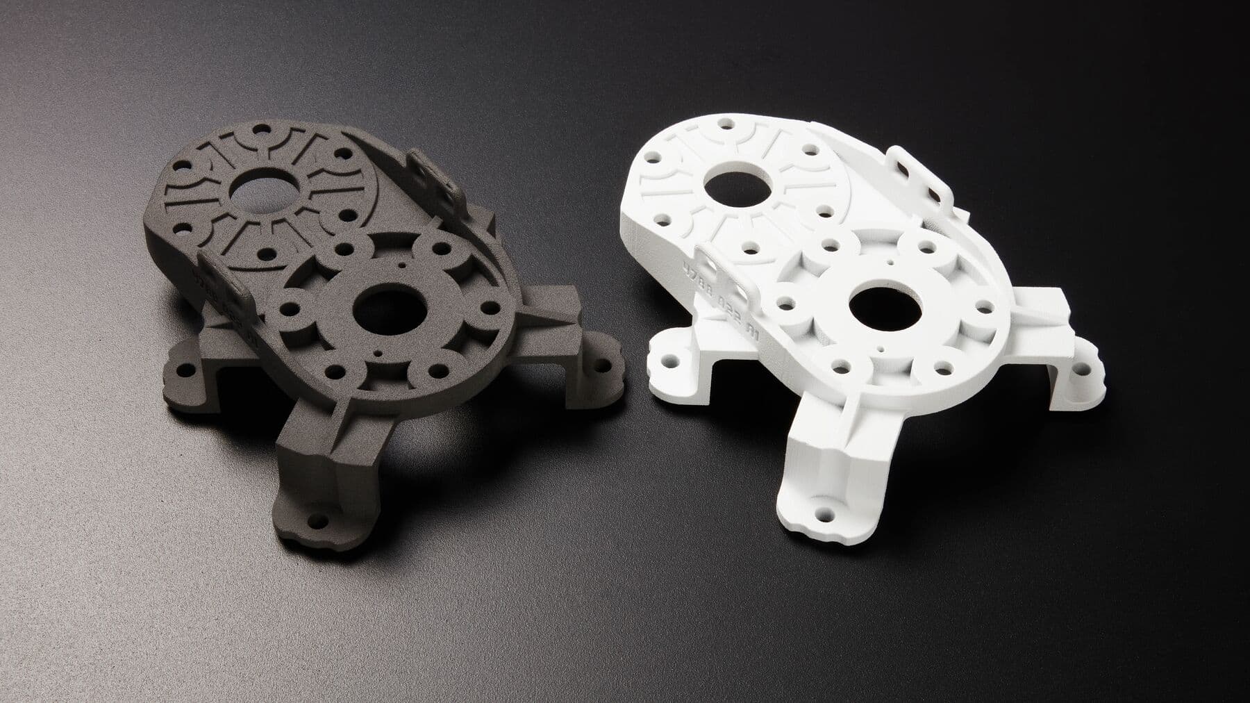 two sls 3d printed parts, automotive swivel gear, one on the left is nylon and dark grey, one on the right is white and cerakoted