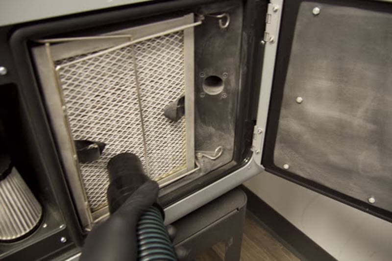 A vacuum hose is being brought to the grate of the exhaust filter