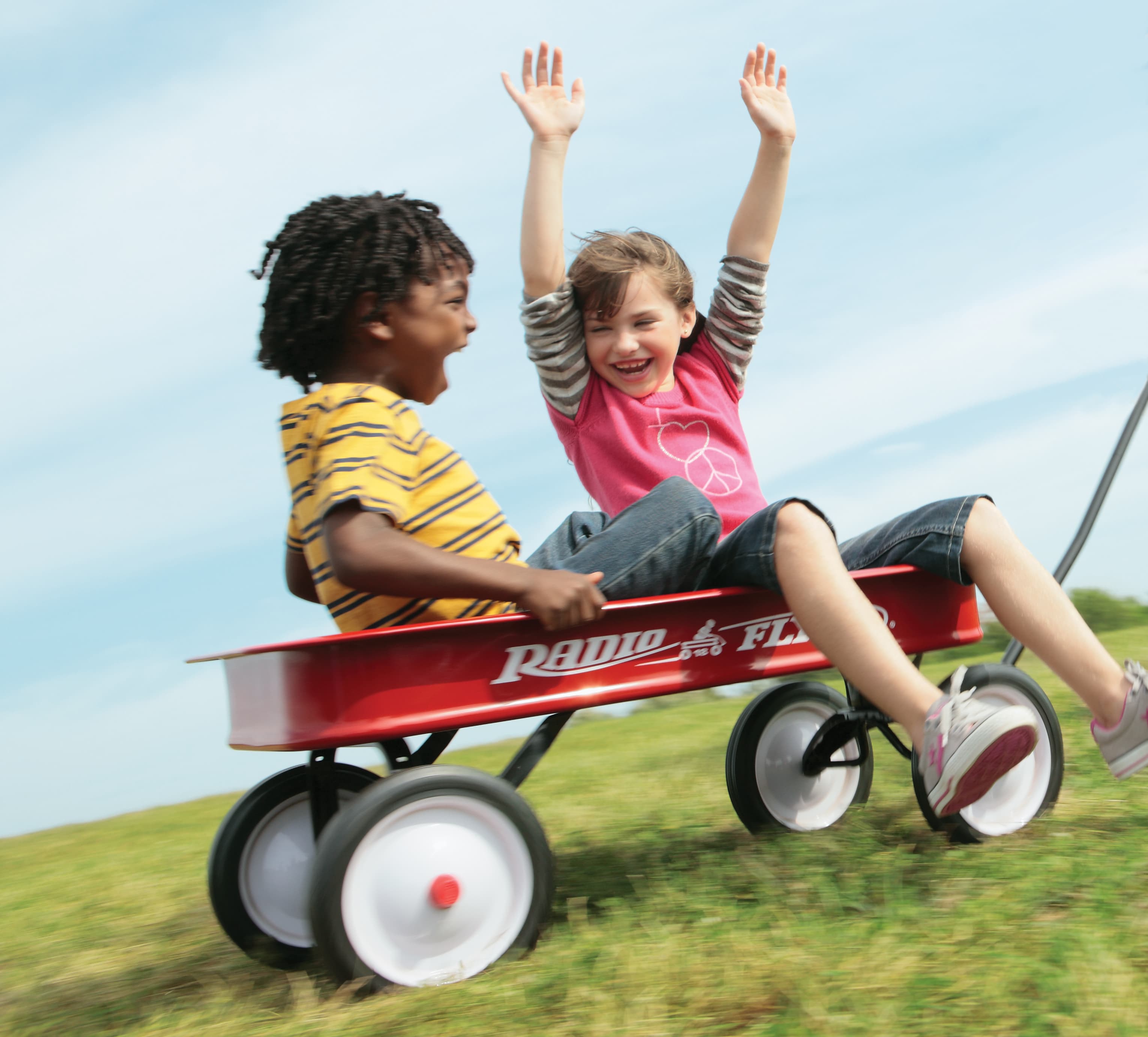 dos niños sentados en una vagoneta roja de radio flyer