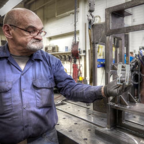 A welder at A&M Tool and Design compares a 3D printed model to the final, full-scale weldment.