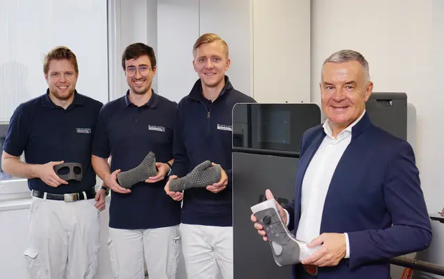 Four people holding orthotics in front of a Fuse 1+ 30W 3D printer