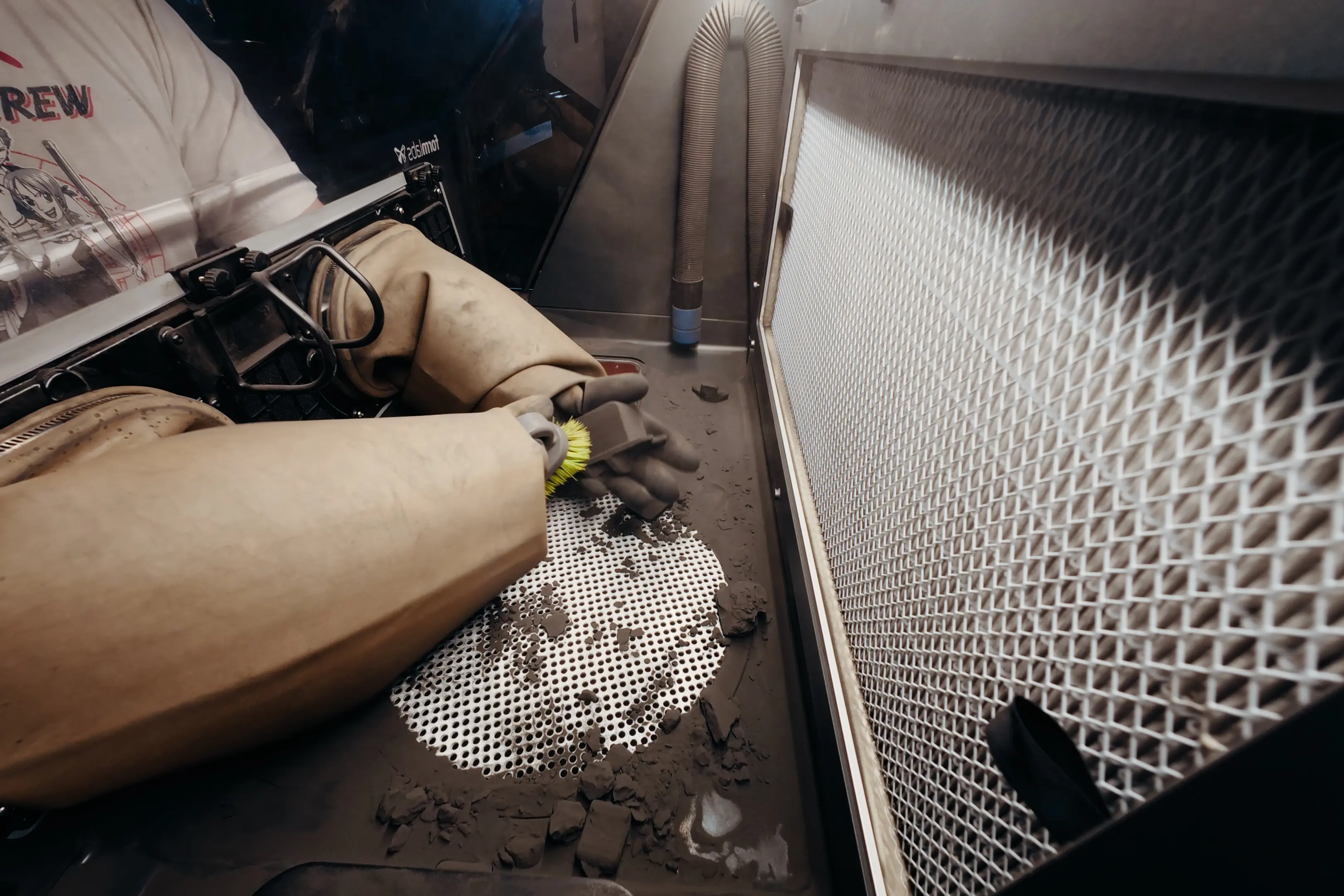 Engineer in protective gear using a brush to clean powder off a 3D-printed component inside the Fuse Sift.