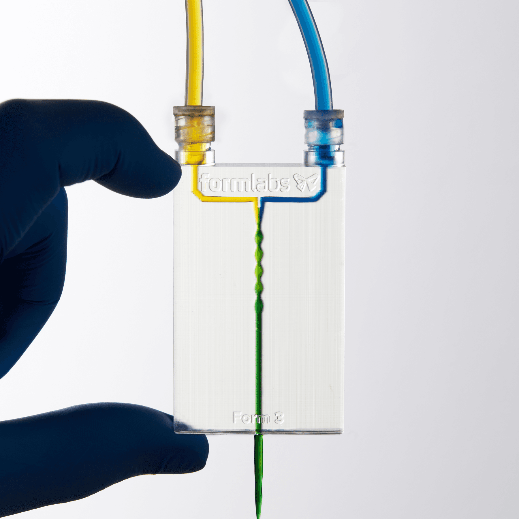 A clear device with 3D channels. Yellow liquid enters through the top left, blue through the top right, and the output is green