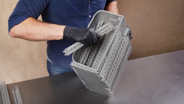 Person wearing a glove pulling bundled supports from inside a large 3D printed part