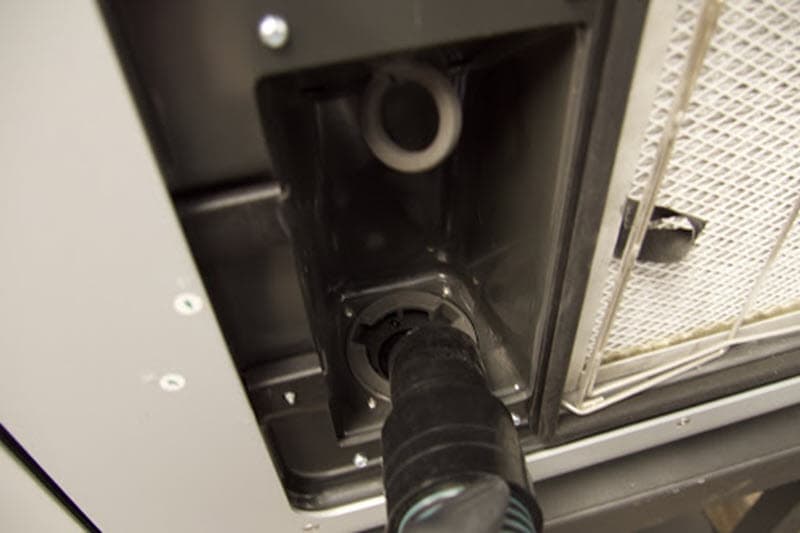 The intake filter has been removed from the cabinet and a vacuum hose is being brought to the resulting cavity