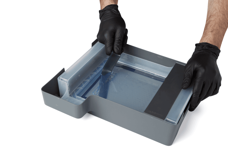A photo showing the entire edge of the tank tool being starting to be dipped underneath the cleaning mesh.