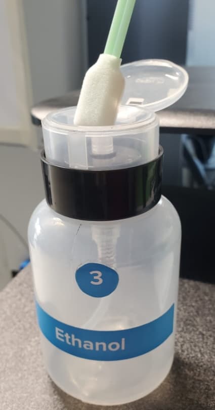 A swab is being pressed against the top of an ethanol dispenser.
