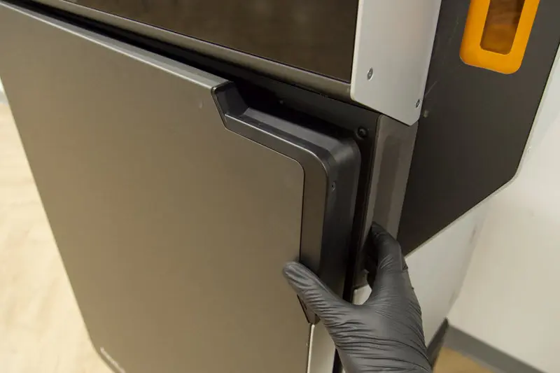 Someone is reaching out to grip the print enclosure door and open it