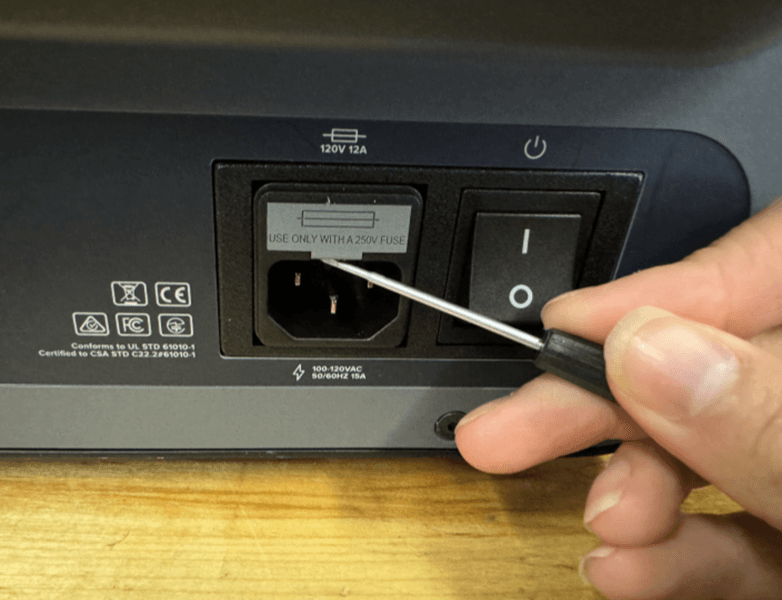 Using a flathead screw driver, gently push up against the fuse box to lever it out of the machine.