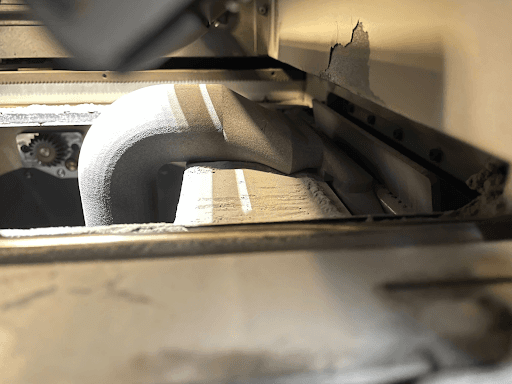 The vacuum attachment enters up through the print enclosure to hook into place and hold up the doser.