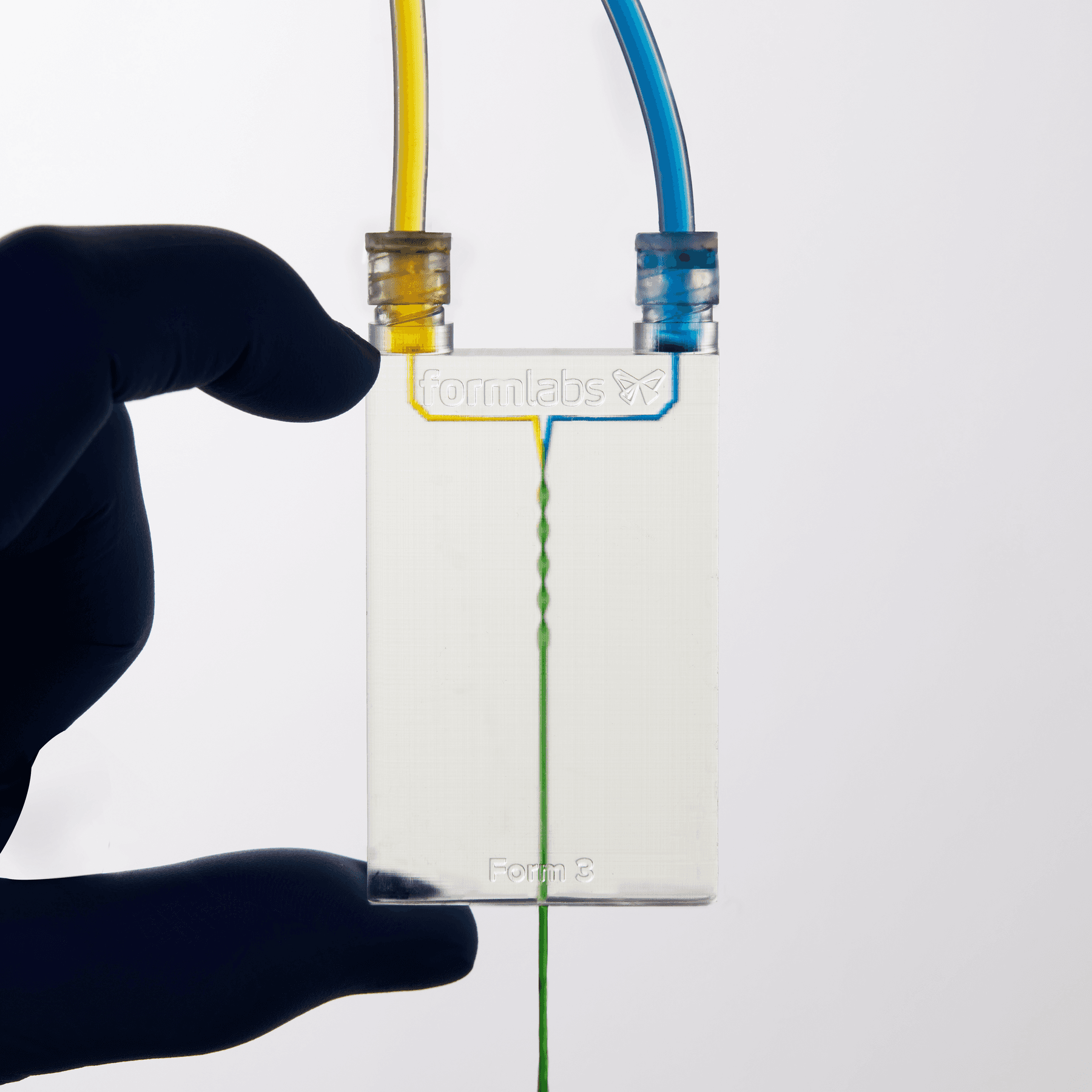 A clear device with 3D channels. Yellow liquid enters through the top left, blue through the top right, and the output is green