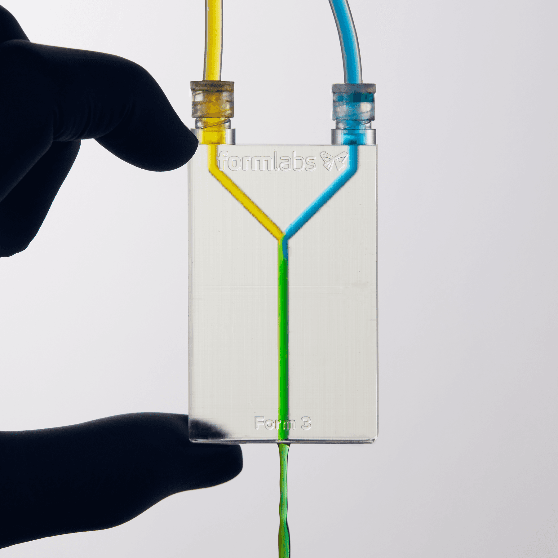 A clear fluidic device with 2.5 mm channels. Yellow liquid enters from top left and blue from top right, mixing to form green