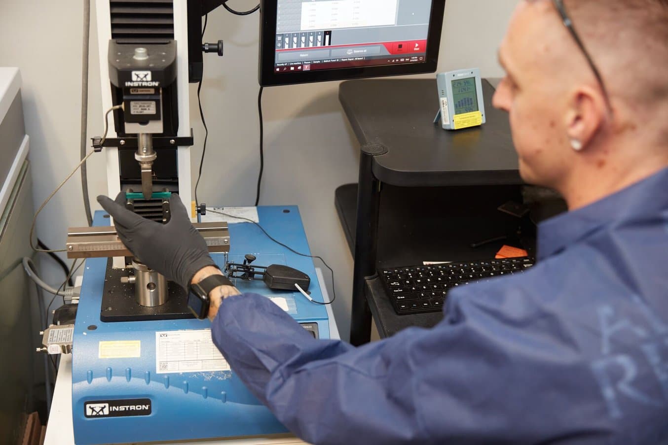 Person with gloves testing a sample with a machine and computer monitor