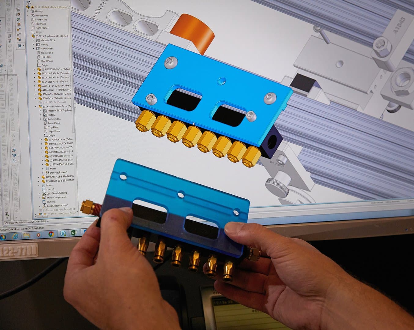 An air manifold mount 3d printed in tough resin in front of a computer screen with the same part in CAD