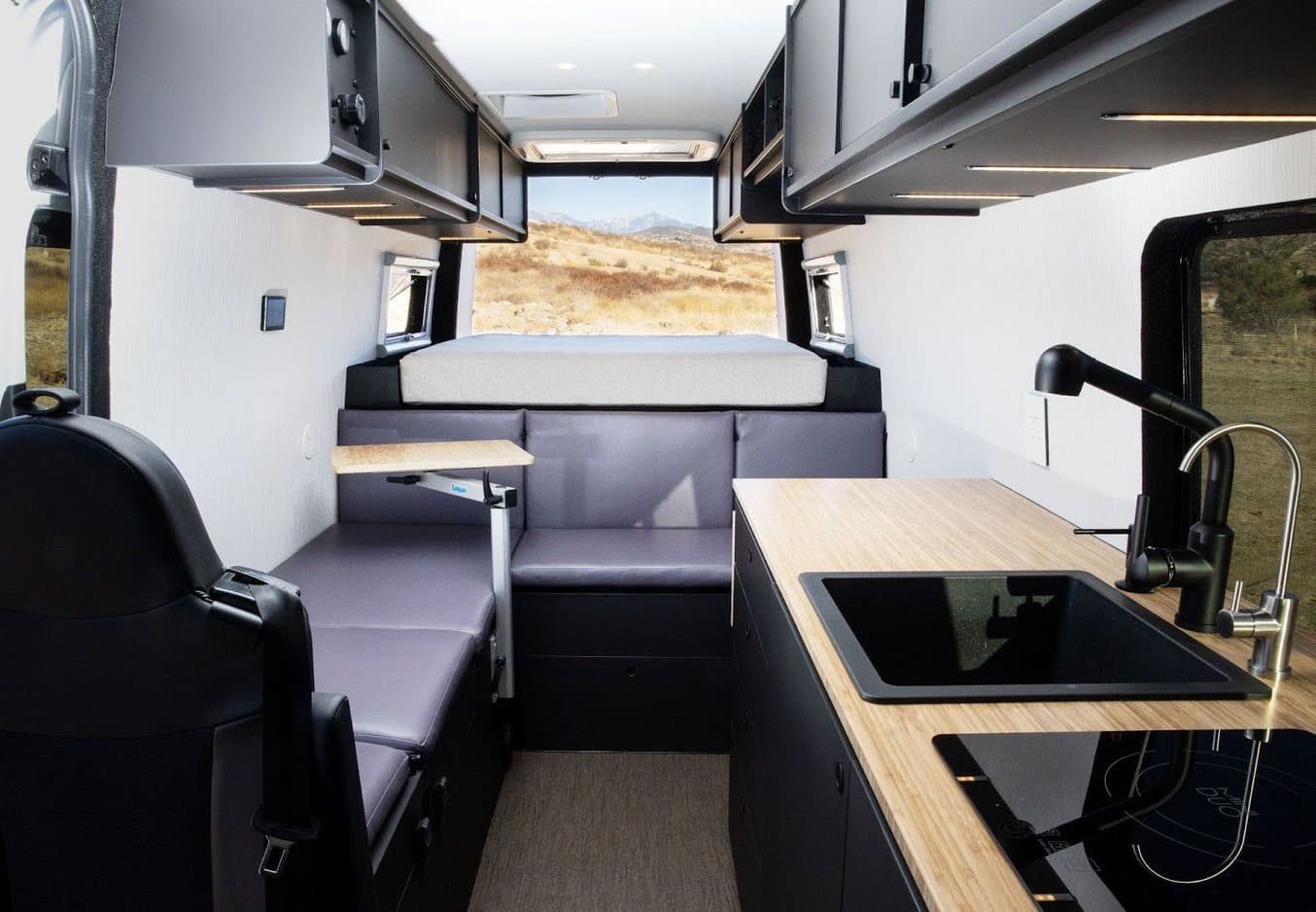 the interior of a van build out with sink, bed, seating, stovetop