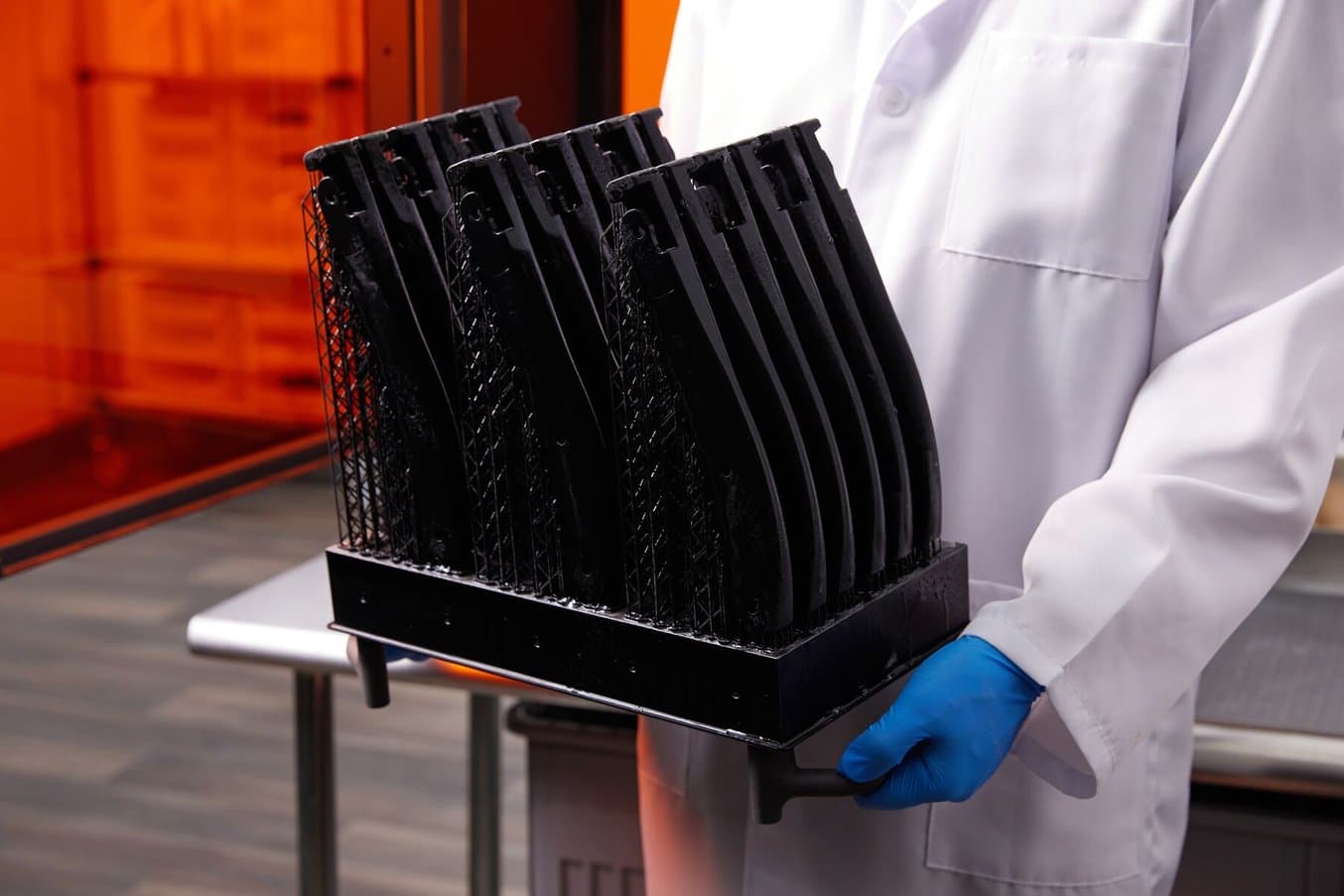 Black 3D printed parts on a Form 4BL Build Platform held by someone wearing gloves