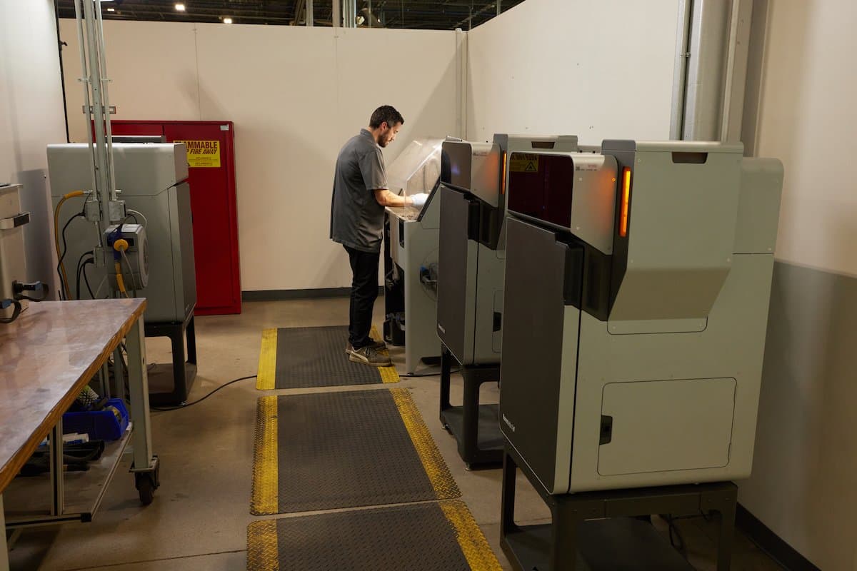 a man stands at the Fuse selective laser sintering SLS 3D printer in a workshop creating end of arm tooling components for automotive robotic systems at Brose