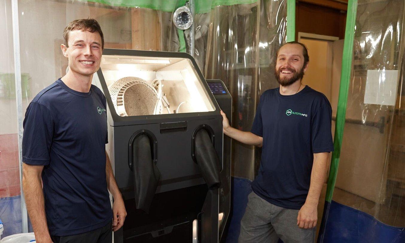 two men stand in front of the Formlabs Fuse Blast, an automated media blasting solution for SLS 3D printed parts