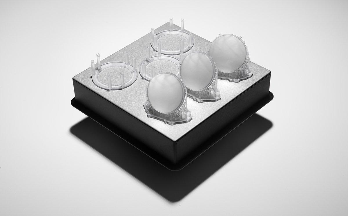 Unfinished 3D printed lenses rest on a build platform after being washed in isopropyl alcohol.