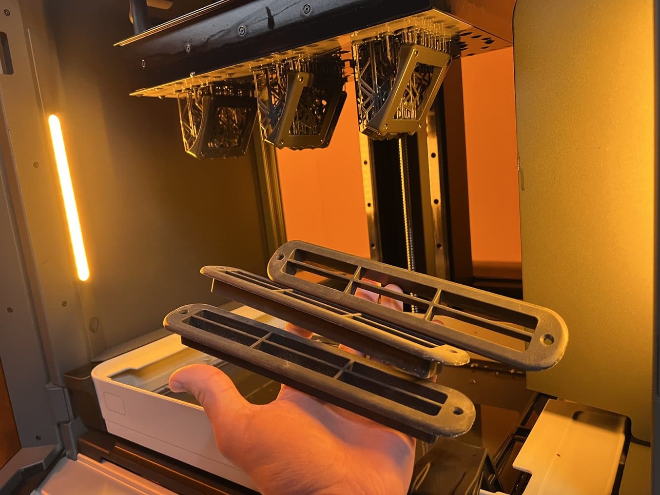Dark grey parts on a build platform inside the Form 4L and a hand holding three finished parts.