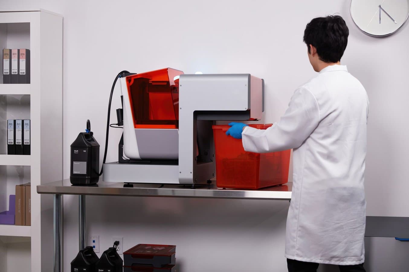 a man in a white lab coat removes parts from the Form Auto, which has the Resin Pumping System inserted into the back