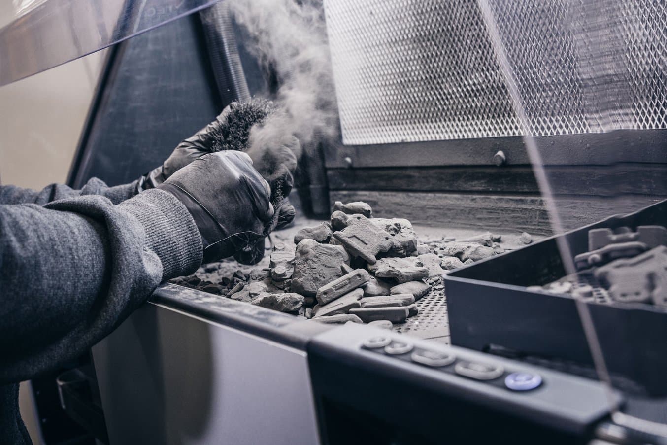 Two hands remove powder from a 3D printed part inside the Fuse Sift post-processing machine.