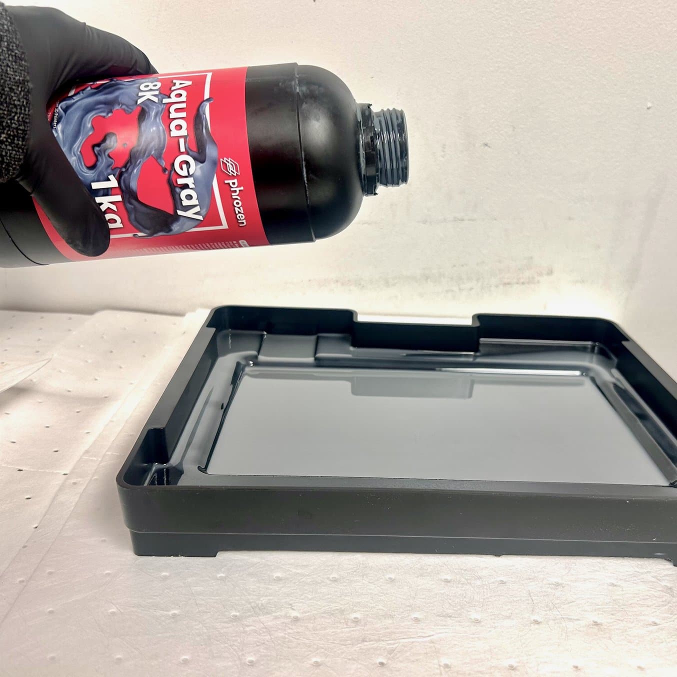 Gloved hand pouring resin into resin tank.