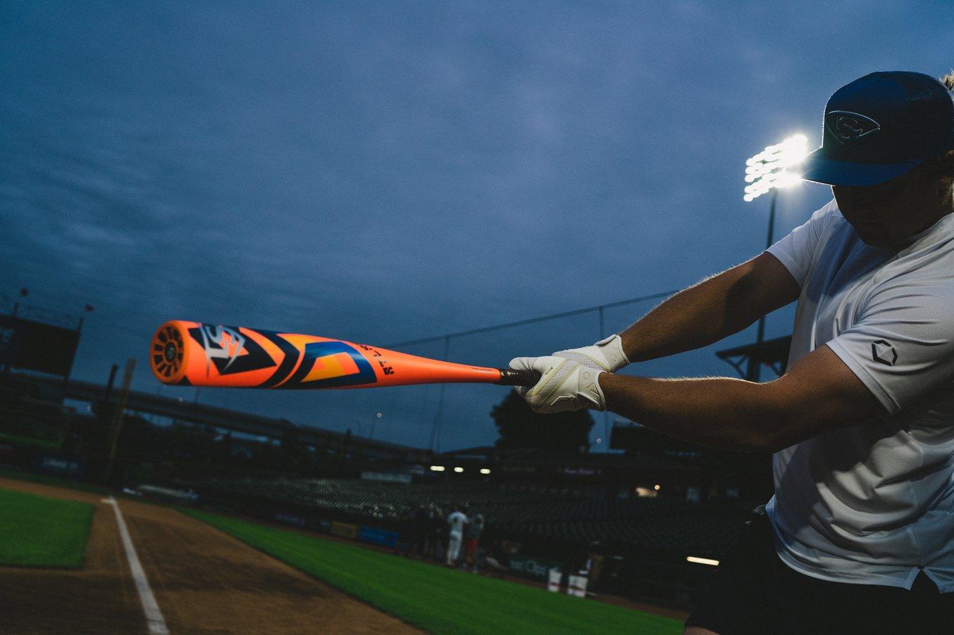 a baseball player swings an orange baseball bat on a baseball field