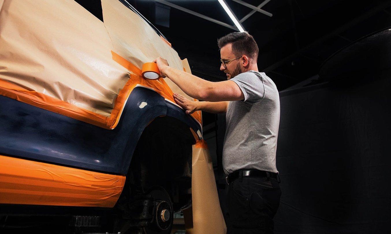 a man uses tape and paper to mask parts of a car body for painting