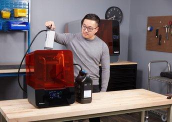 a man stands to the side of the Form 3 stereolithography (SLA) 3D printer using the Resin Pumping System