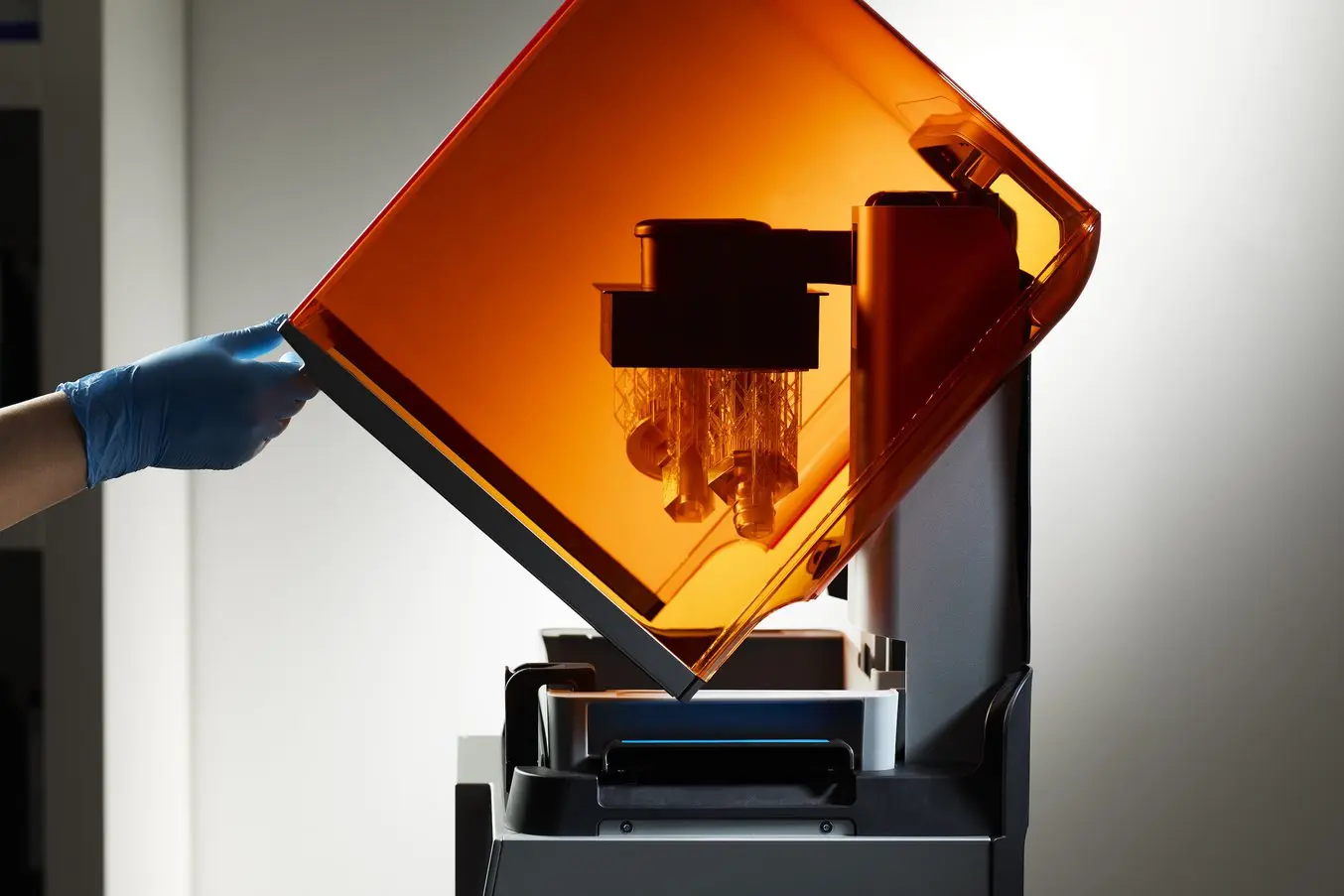 una mano con un guante azul levanta la cubierta naranja de una impresora 3D Form 4