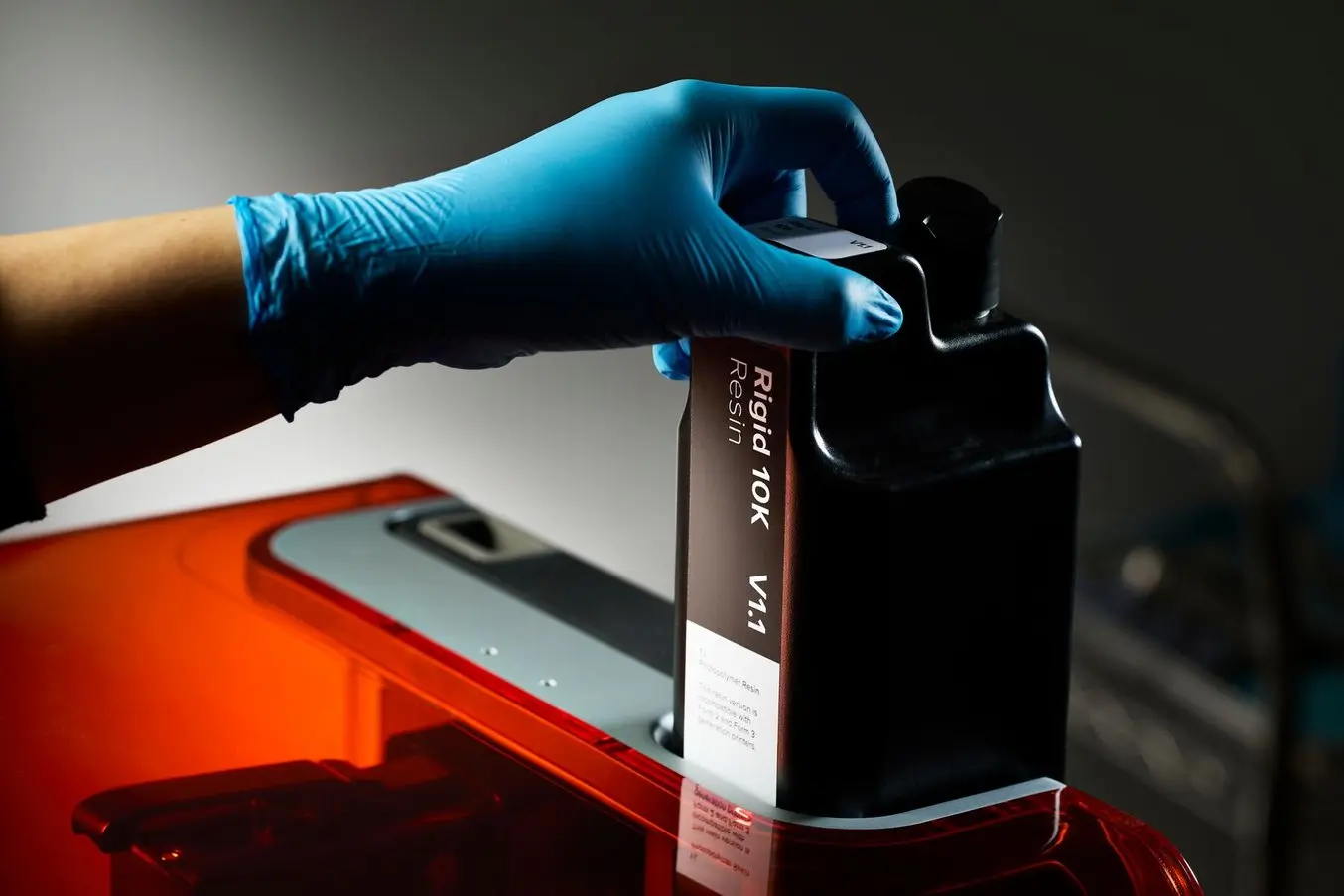 a blue gloved hand inserts a resin cartridge into the back of the Form 4 3D printer