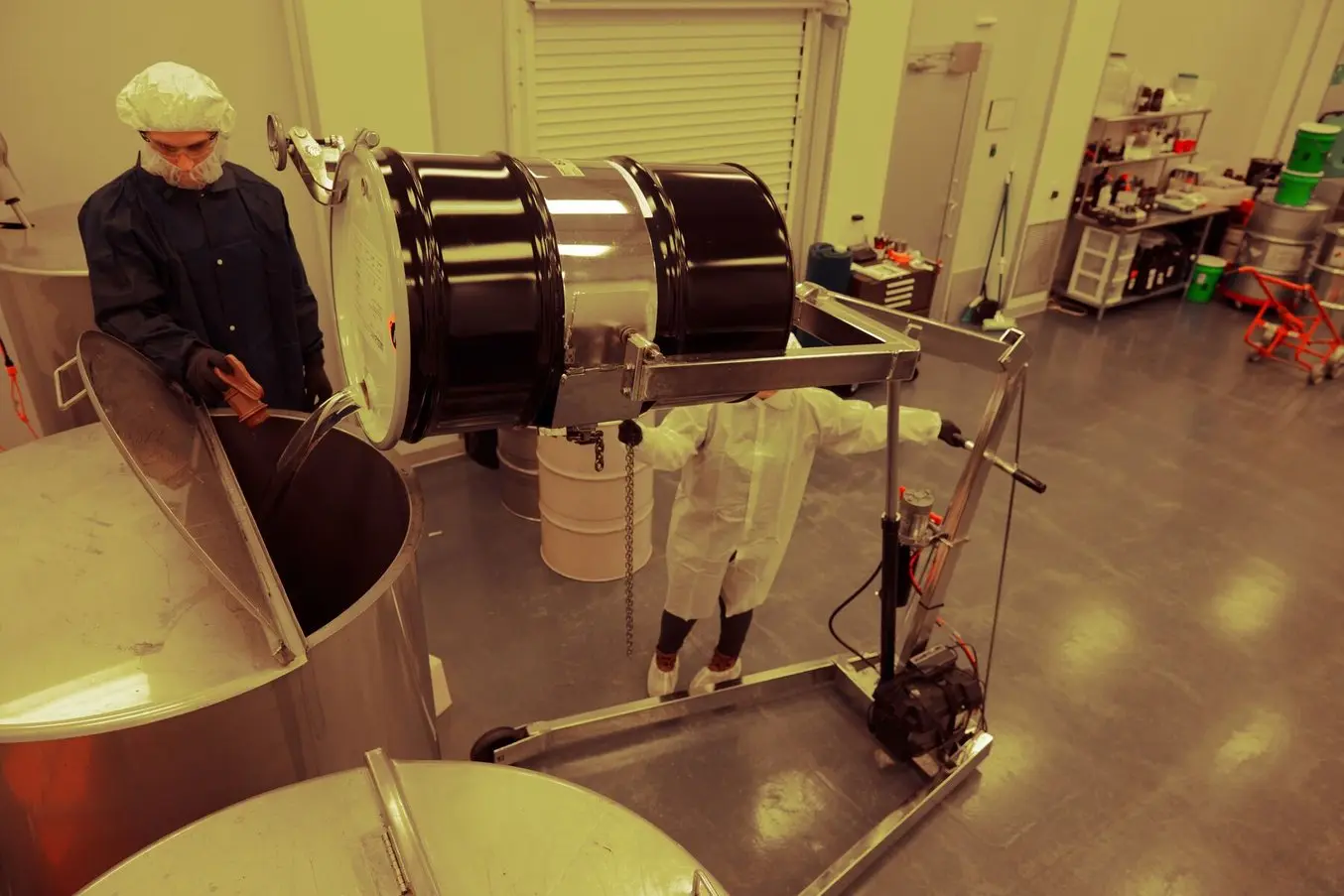 Two people in PPE pouring material from one barrel to another