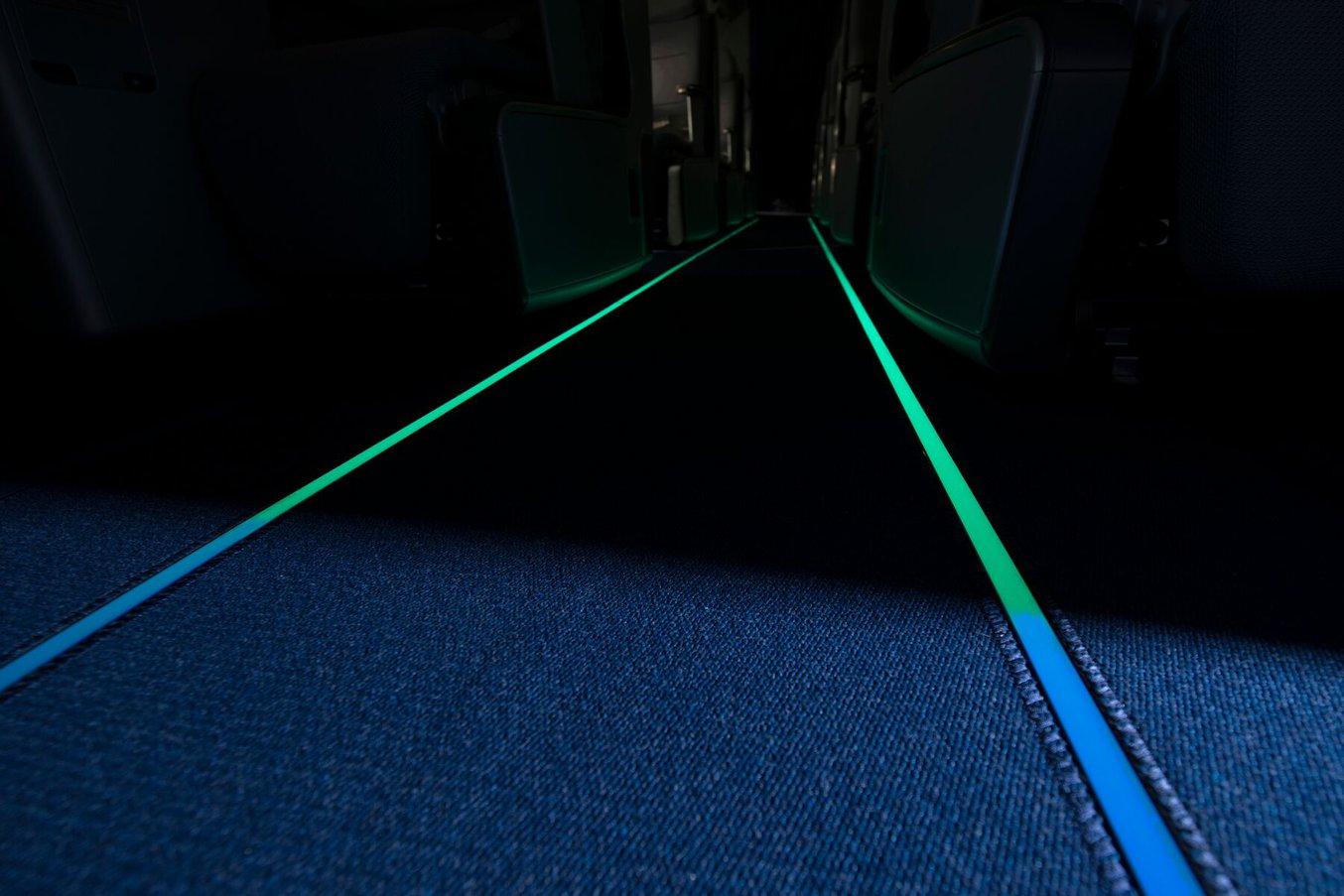 Vue de l'intérieur d'un avion avec des marquages luminescents bleus et verts de voies d'évacuation.