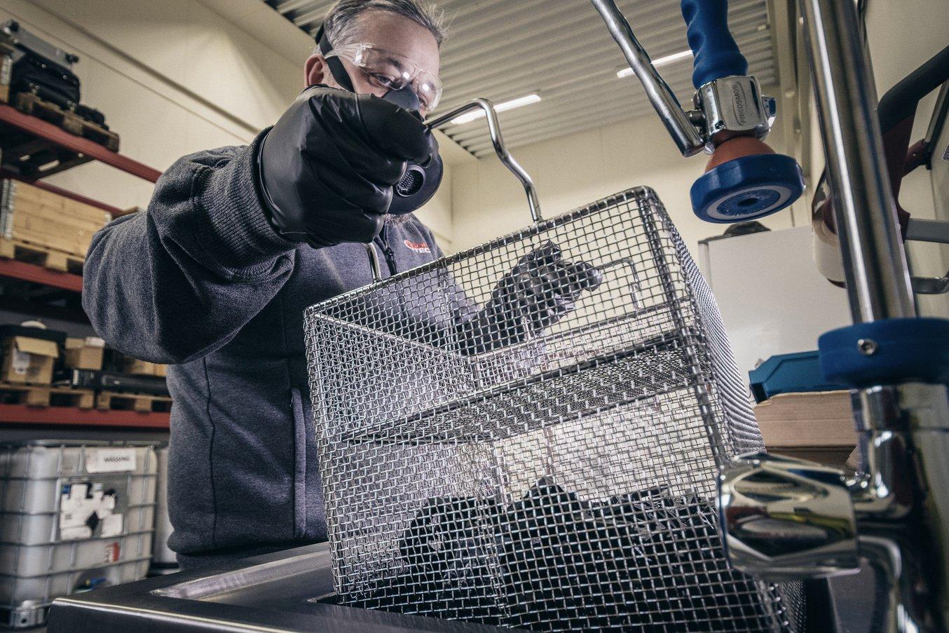 A man lifts a wire basket containing 3D printed parts out from a holding area.