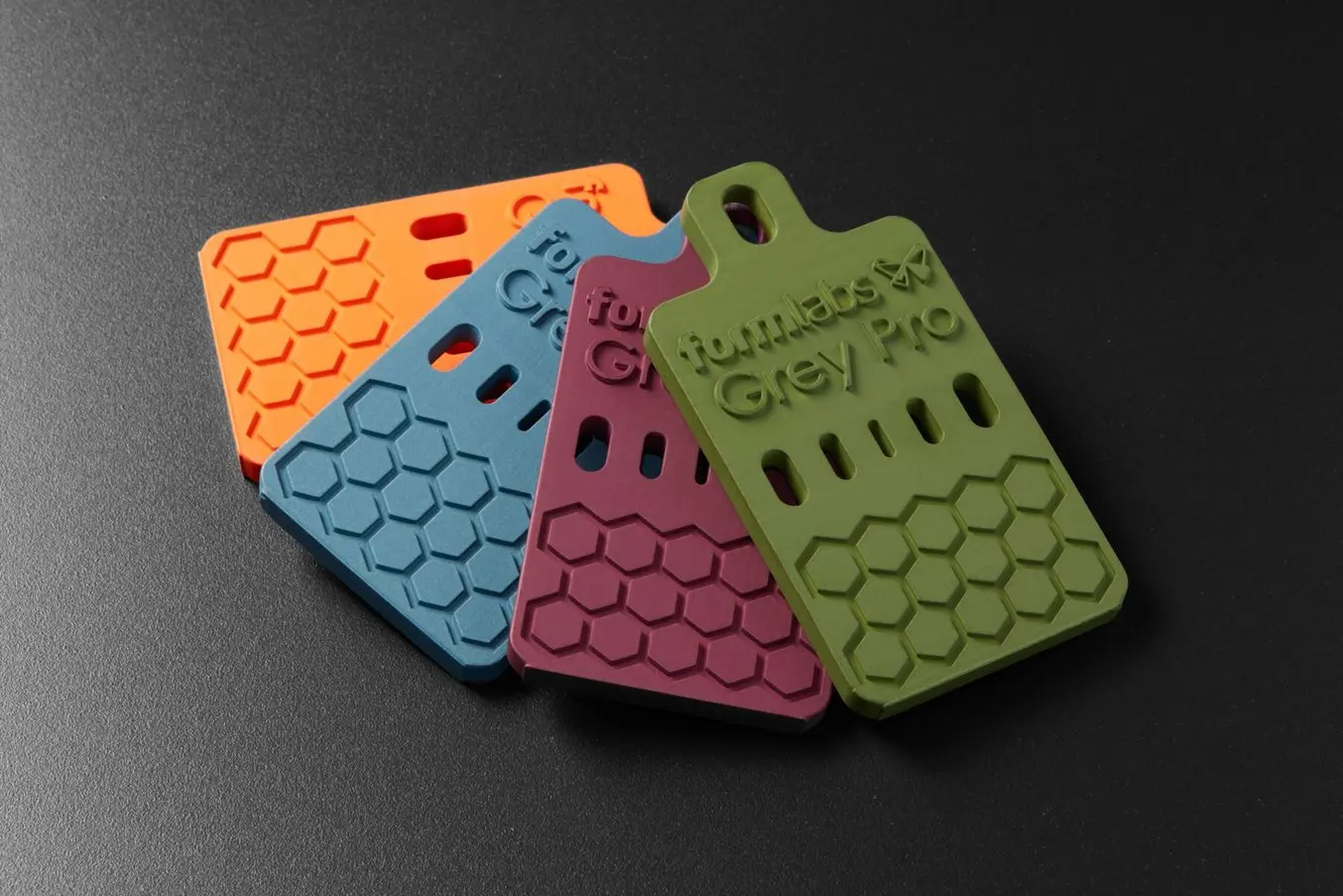 cuatro objetos pequeños con forma de tarjeta, impresos en 3D en la impresora de estereolitografía (SLA) Form 3+ con la Grey Pro Resin y revestidos con Cerakote en naranja, azul, rojo y verde